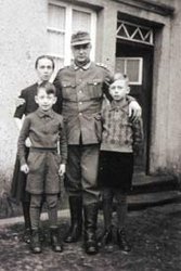 Photographie von Heinz Wilhelmy in Wehrmachtsuniform vor seinem Haus seine Arme um seine Frau und einen Sohn  gelegt. Sein zweiter Sohn steht vor seiner Frau.